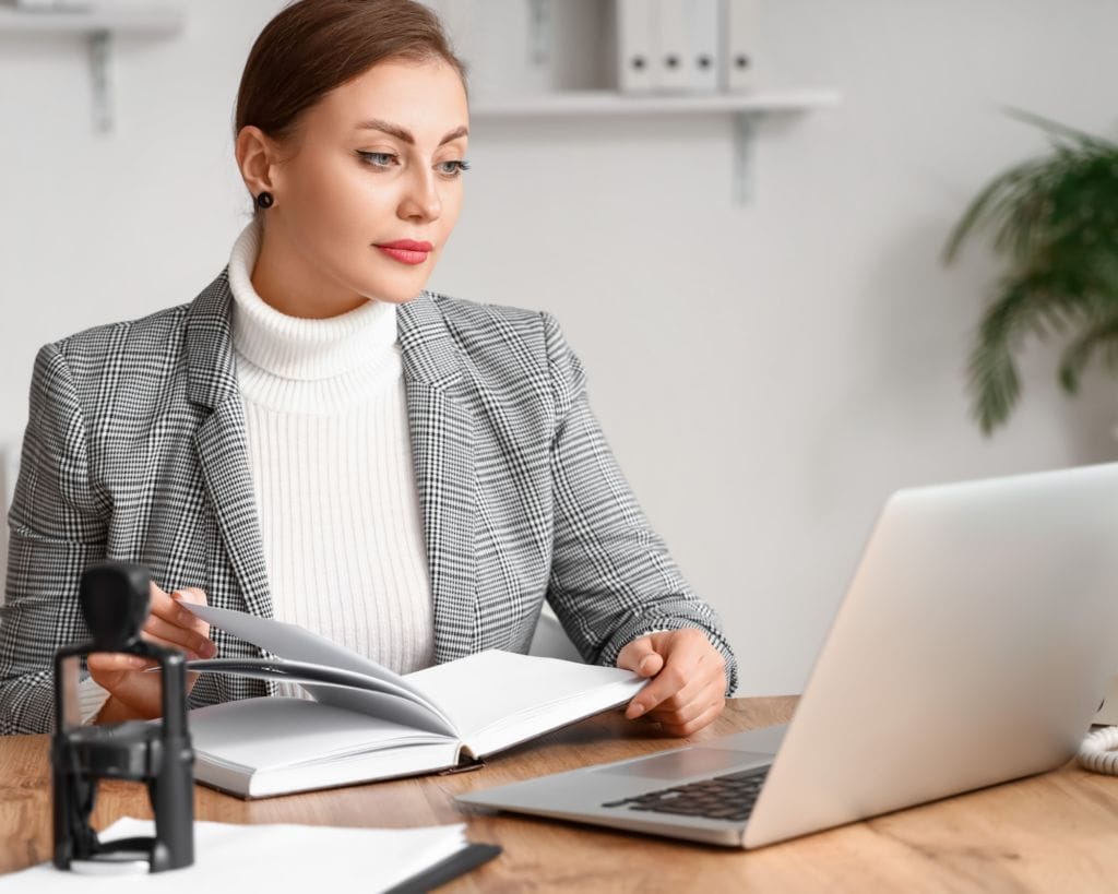 Prestige Notaries - A woman sitting at a desk with a laptop providing seamless notary services. 